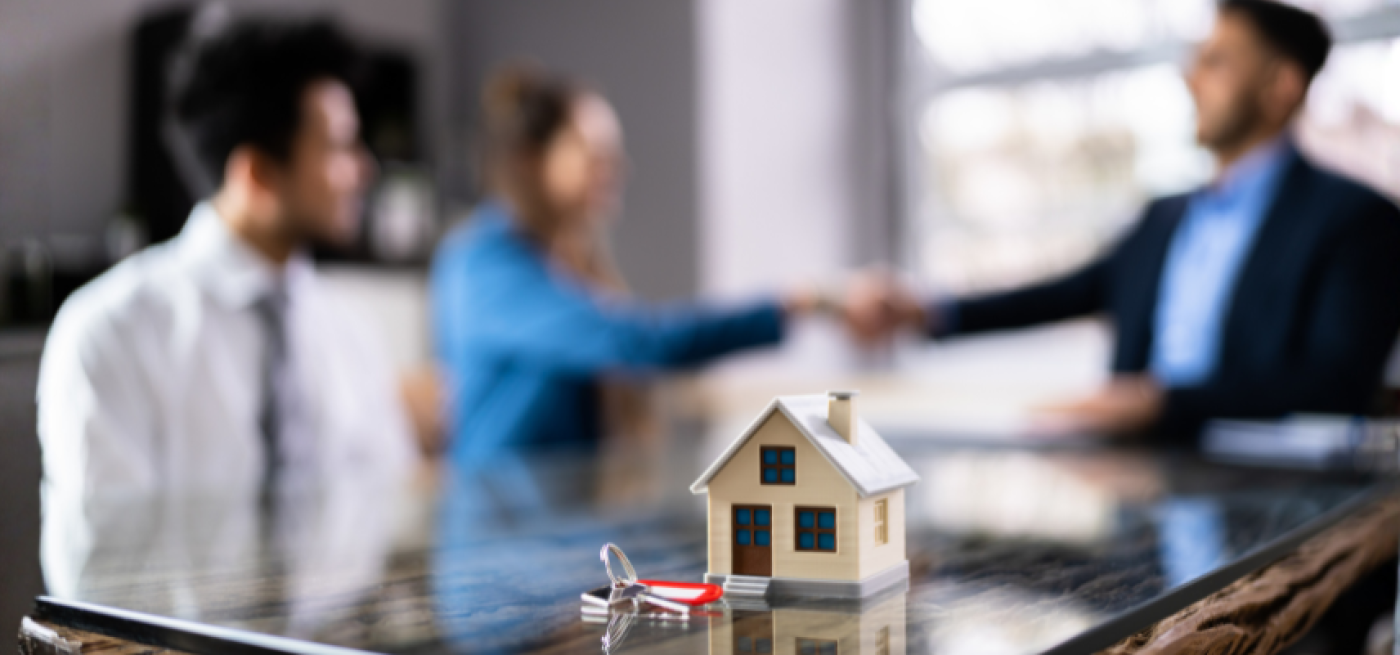 Intermediário de crédito a apoiar um casal na compra de casa, com chave e maquete de habitação sobre a mesa, representando o crédito habitação.